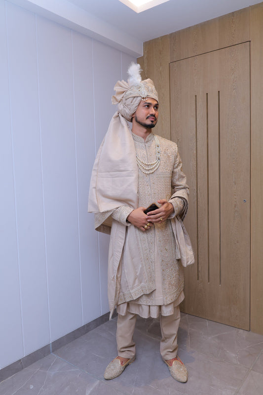 Person in a beige outfit standing on a white floor with a wooden panel in the background