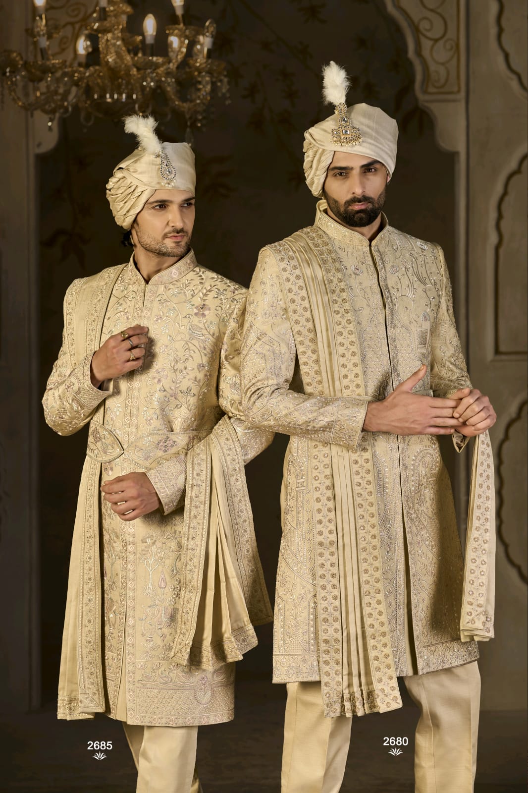 Two men in traditional cream-colored sherwanis with turbans standing against a dark background.