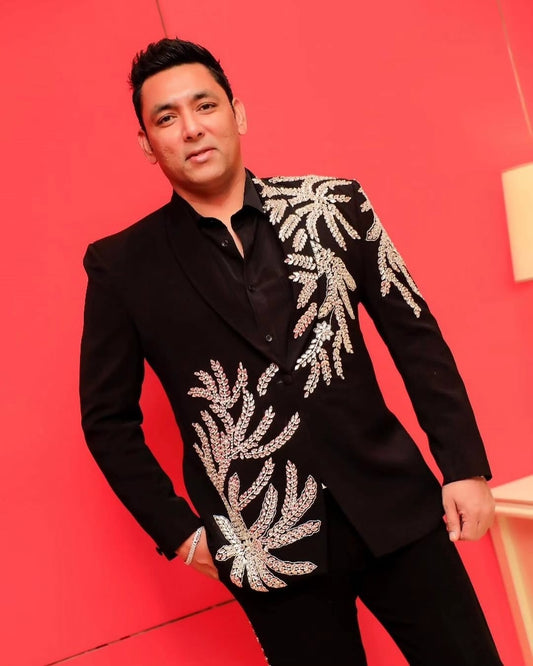 Man wearing a black suit with silver leaf patterns against a red background