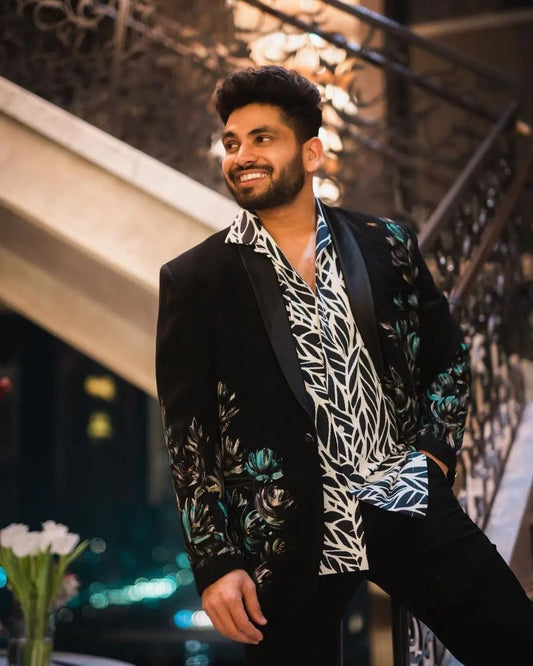 Man wearing a stylish black blazer with floral patterns and a patterned shirt in an indoor setting.