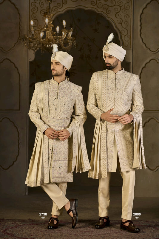 Two men in traditional embroidered sherwanis standing against a decorative wall.