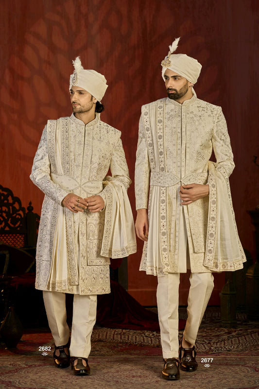 Two men in traditional embroidered sherwanis with turbans against a red background