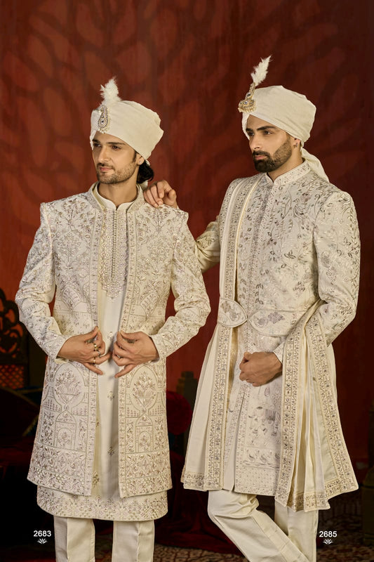 Two men in traditional embroidered sherwanis with turbans against a dark background