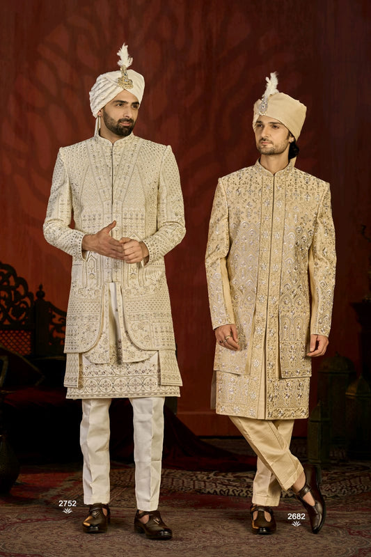 Two men in traditional embroidered sherwanis with turbans against a red background