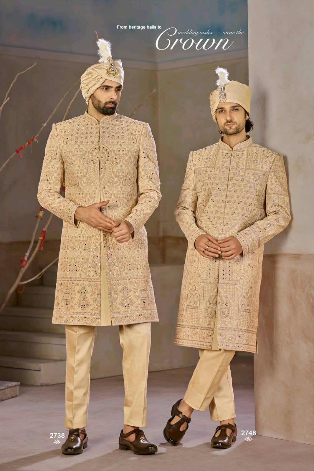 Two men in traditional embroidered sherwanis with decorative turbans indoors.