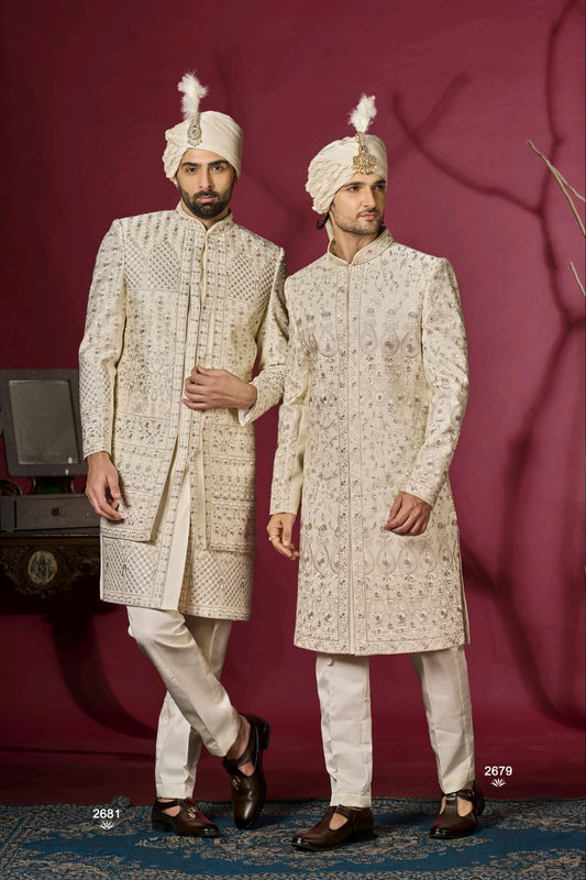Two men in traditional embroidered sherwanis standing against a red background