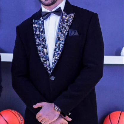 Two men in formal attire standing in front of a branded backdrop with sports balls.