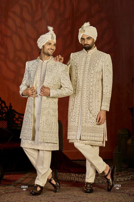 Two men in traditional embroidered sherwanis standing against a red background