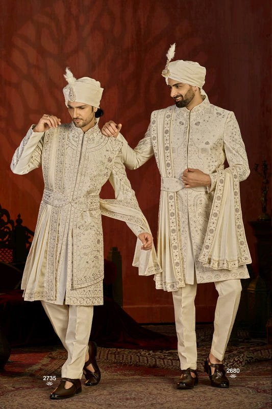 Two men in traditional embroidered sherwanis with turbans against a red background